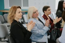 Три жінки сидять у залі та аплодують.