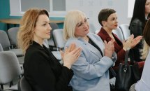 Три жінки сидять у залі та аплодують.