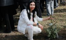 Жінка у білому одязі сидить біля саджанця ялинки.