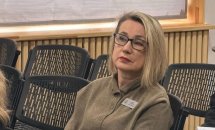 Фото жінки у коричневій кардигані, що сидить на стільці у залі.