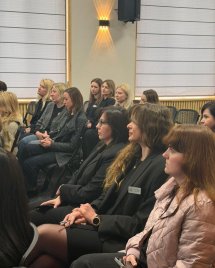 Групове фото жінок, що сидять на стільцях у залі.