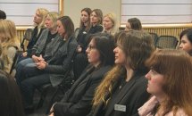 Групове фото жінок, що сидять на стільцях у залі.