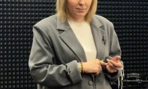 Жінка у сірому піджаку на фоні стіни.