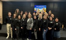 Групове фото у залі на фоні стіни.