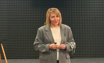 Жінка у сірому піджаку на фоні звукоізолюючої стіни