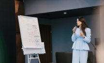 Жінка у блакитному костюмі щось розповідає у мікрофон.