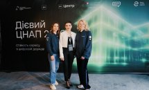 Три жінки позують на фоні банера.