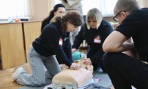 Дівчина робить непрямий масаж серця на манекені, жінка збоку робить вентеляцію легень.