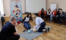 Дві жінки стоять на колінах біля манекена, збоку сидить чоловік.