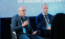 Чоловік тримає мікрофон у руках, біля нього сидить ще один чоловік.