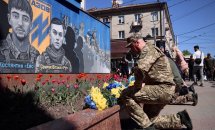 Чоловік у військовій формі стоїть на одному коліні перед муралом.