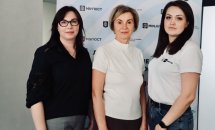 Три жінки позують на фоні банера.