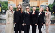 Шість жінок у діловому одязі з маками позують для спільного фото.