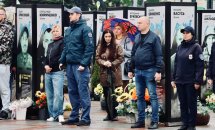 Люди стоять надворі, позаду портрети.