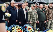 Чоловіки з червоними маками на одязі, перед ними стоять корзини з квітами.