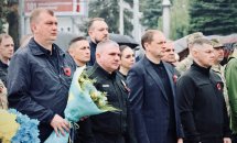 Група людей перебуває надворі, чоловік тримає букет у руках.