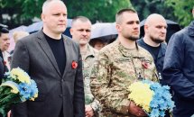 Двоє військових та декілька чоловіків у чорному одязі стоять надворі.