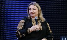 Жінка у чорній вишиванці тримає мікрофон у руках.