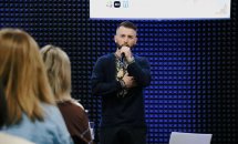Чоловік у вишитій сорочці тримає мікрофон.