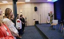 Чоловік у військовій формі тримає мікрофон, жінки стоять перед ним.
