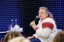 Жінка старшого віку у вишиванці тримає мікрофон у руках.