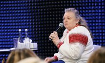 Жінка старшого віку у вишиванці тримає мікрофон у руках.