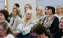 Група жінок у вишитих сорочках сидять у залі.