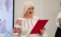 Жінка у вишиванці тримає червону папку.