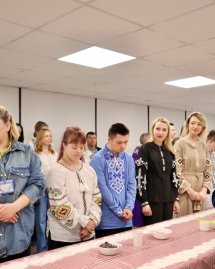 Люди у вишитих сорочках стоять біля столу.
