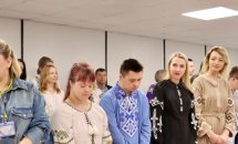 Люди у вишитих сорочках стоять біля столу.