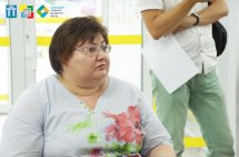 Жінка в білій футболці сидить у залі.