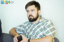 Бородатий чоловік у картатій сорочці сидить схрестивши руки.