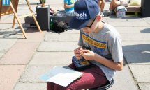 Хлопчик в окулярах та головному уборі малює надворі.