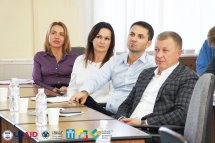 Дві жінки та двоє чоловіків сидять за столом у приміщенні.