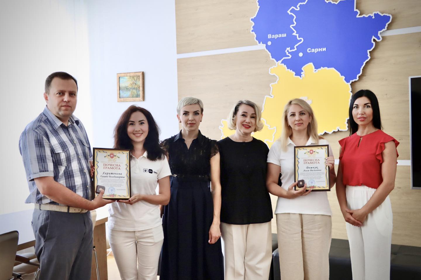 Шестеро людей стоять разом. Дві жінки в центрі тримають почесні грамоти. На одній з грамот написано 'Харитонова Галини Володимирівни'.