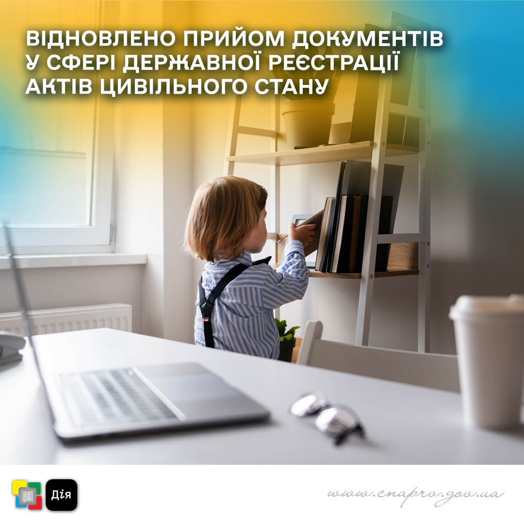 Дитина бере книгу. На передньому плані видно робочий стіл із ноутбуком, окулярами та чашкою.