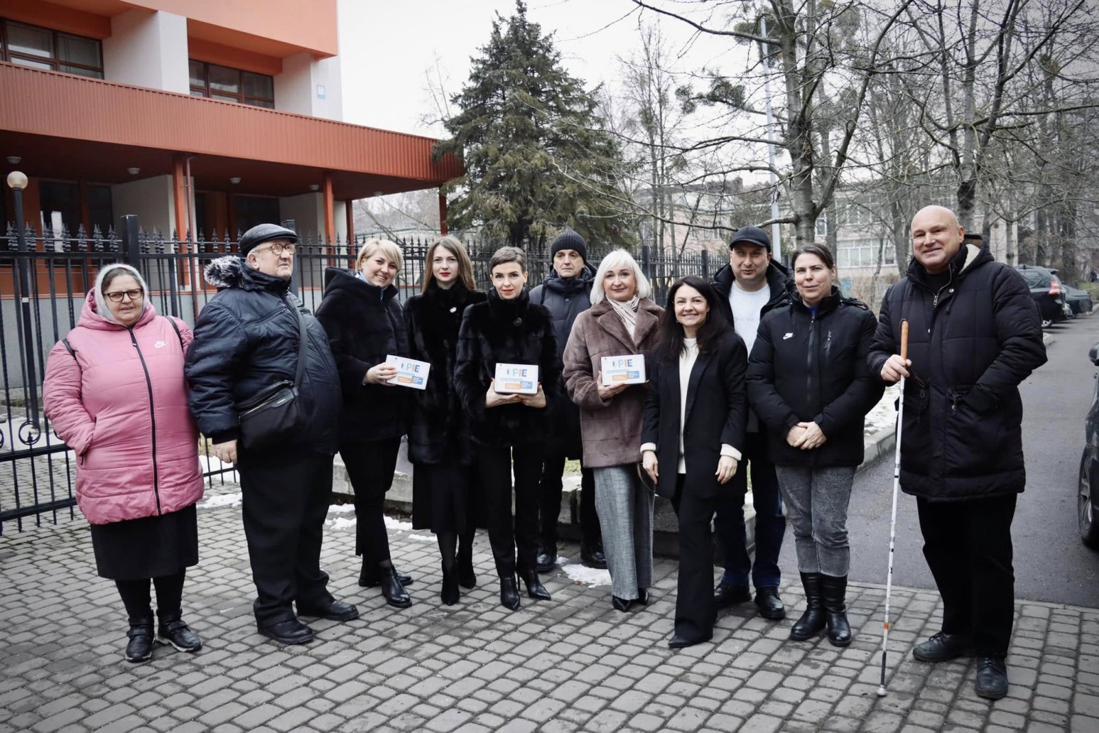 На фото зображено групу людей, які стоять біля будівлі, на вулиці.