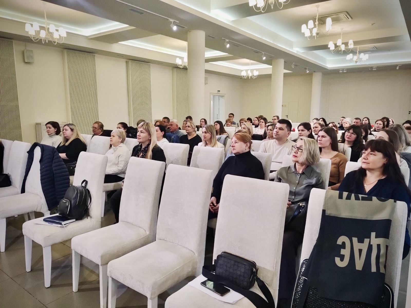 Багато людей сидять у світлому приміщенні. 