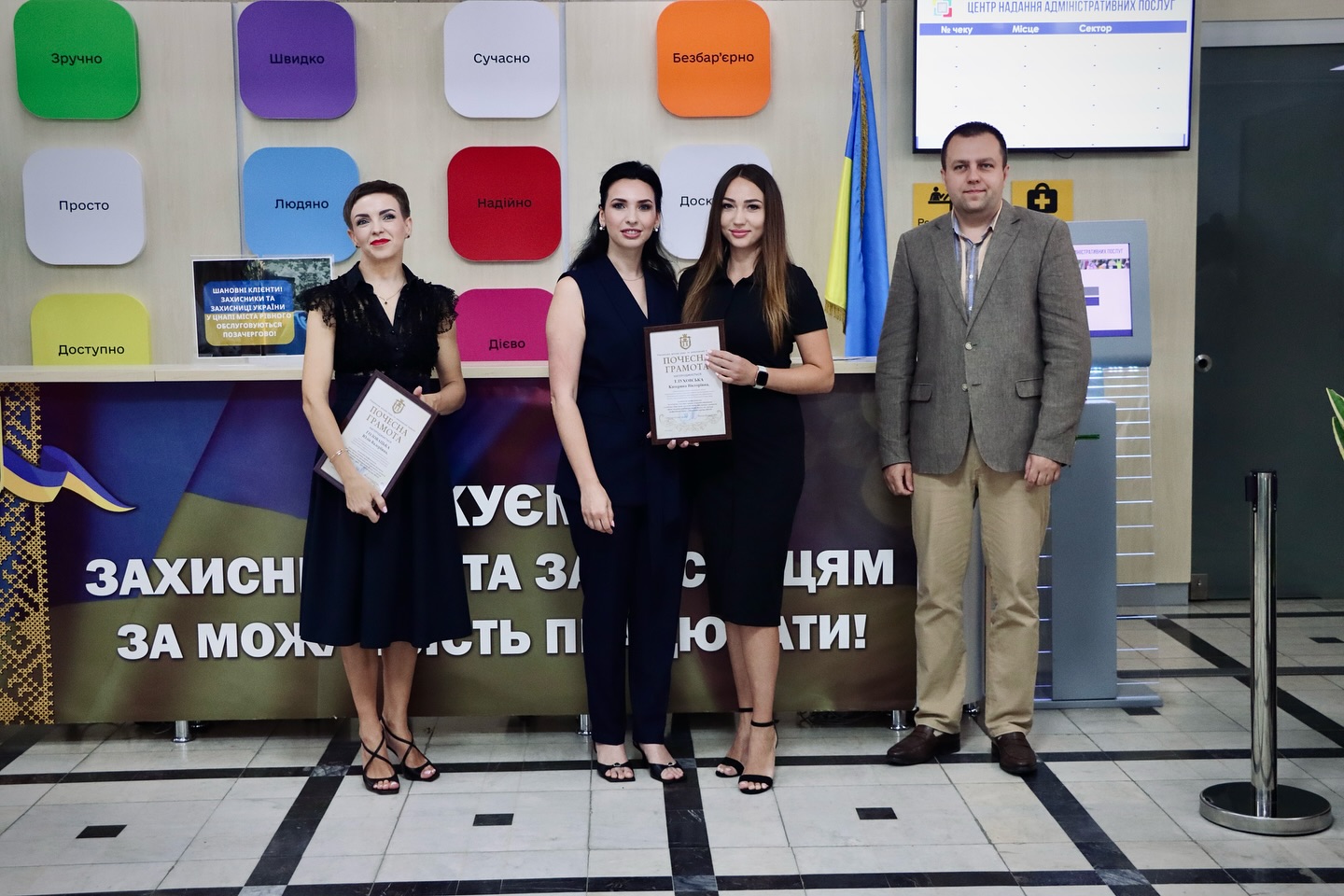 Троє жінок в чорному одязі та чоловік позують для фото, дві жінки тримають грамоти.