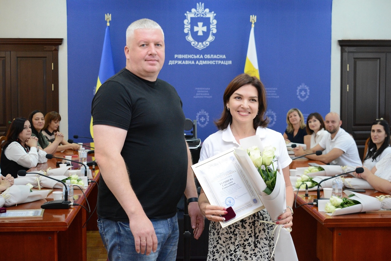 Чоловік та жінка позують для фото з грамотою та квітами.