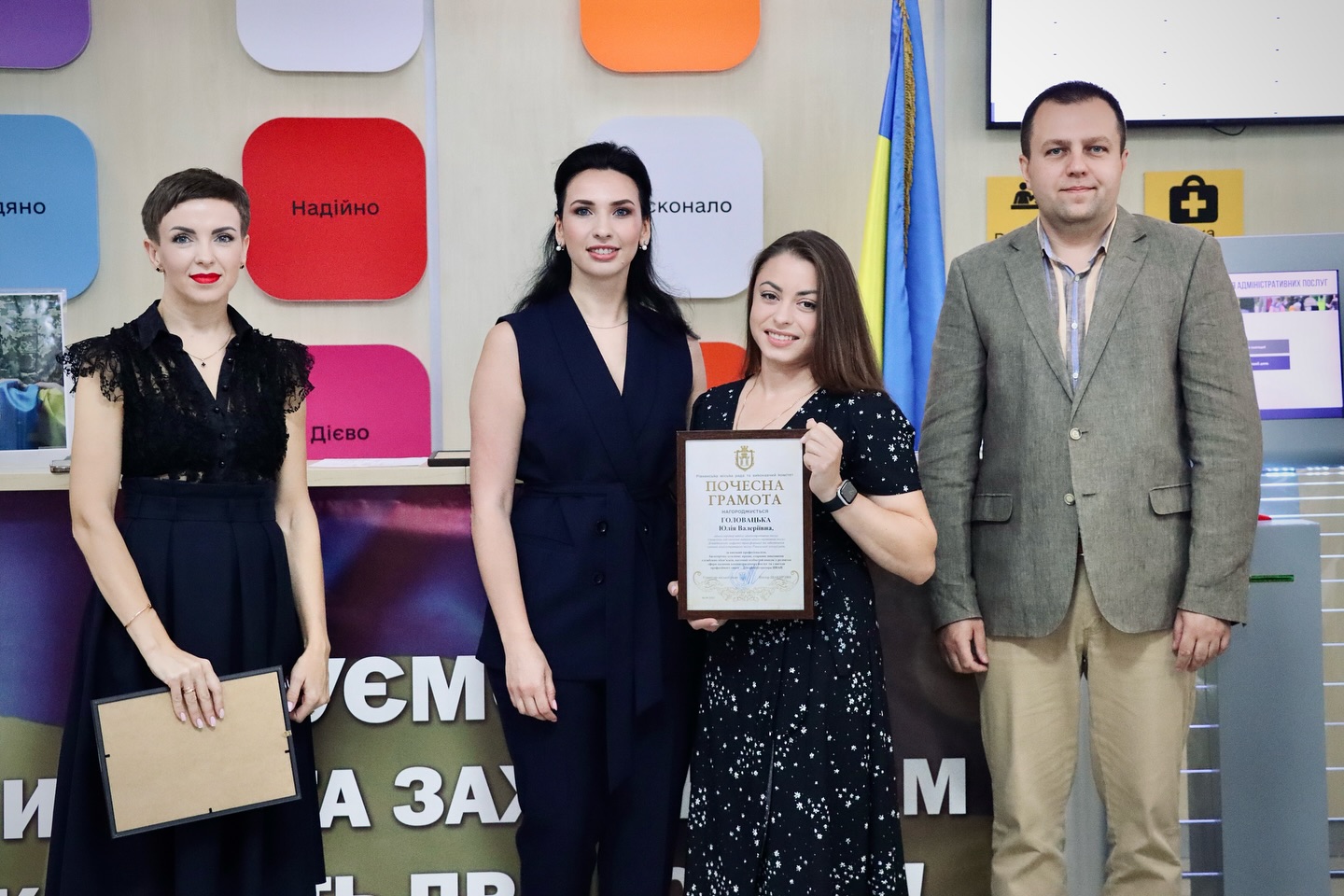 Троє жінок в темному одязі та чоловік позують для фото, дві жінки тримають грамоти.