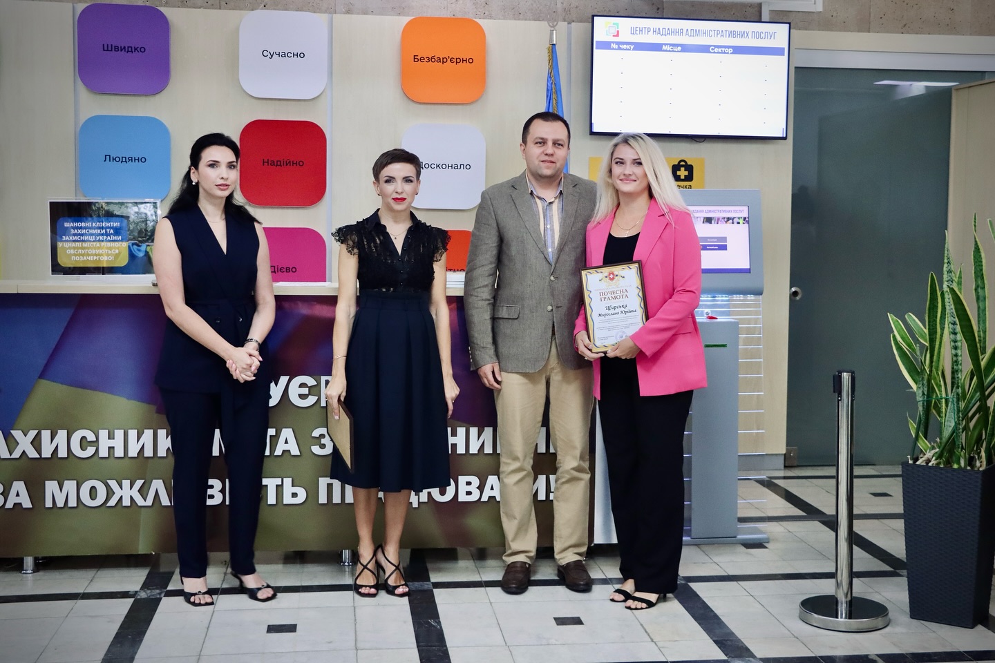 Три жінки та чоловік позують для фото, одна жінка тримає грамоту.