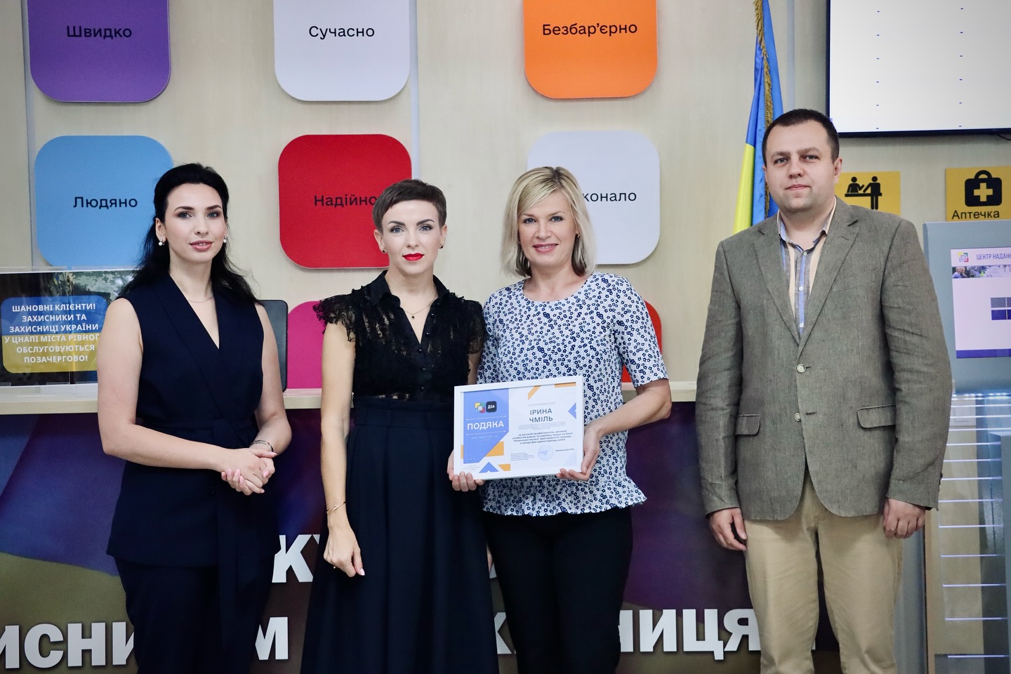 Три жінки та чоловік позують для фото, одна жінка тримає подяку.