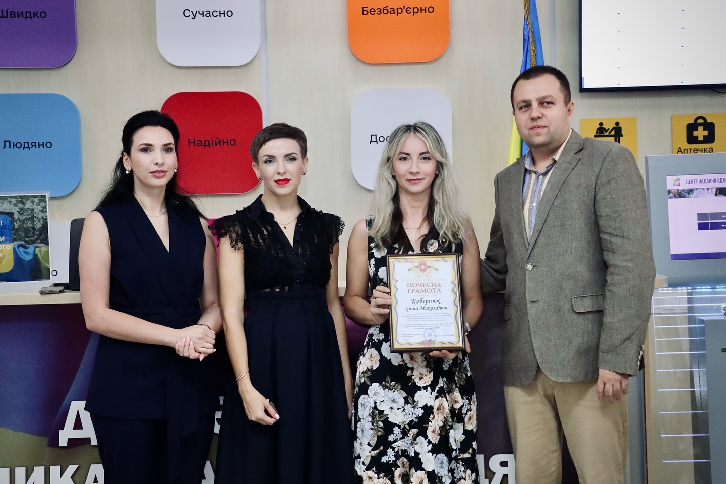 Три жінки та чоловік позують для фото, одна жінка тримає грамоту.