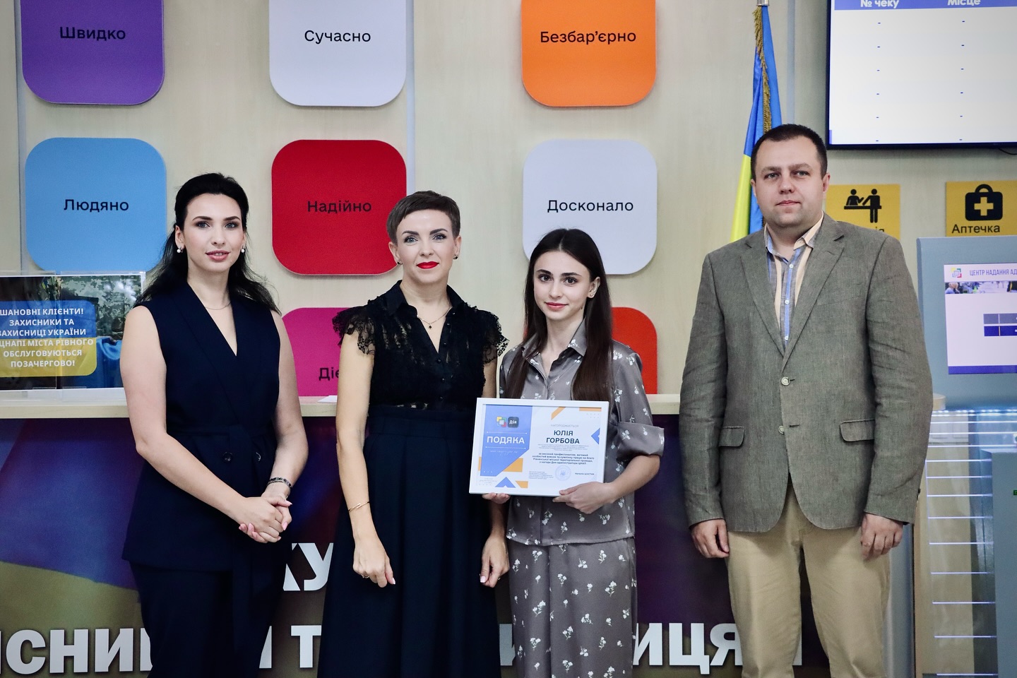 Три жінки в темному одязі та чоловік позують для фото, одна жінка тримає подяку.
