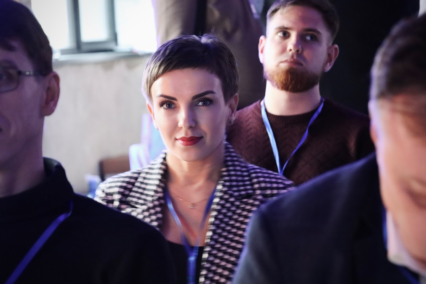 Жінка з коротким волоссям сидить серед чоловіків.