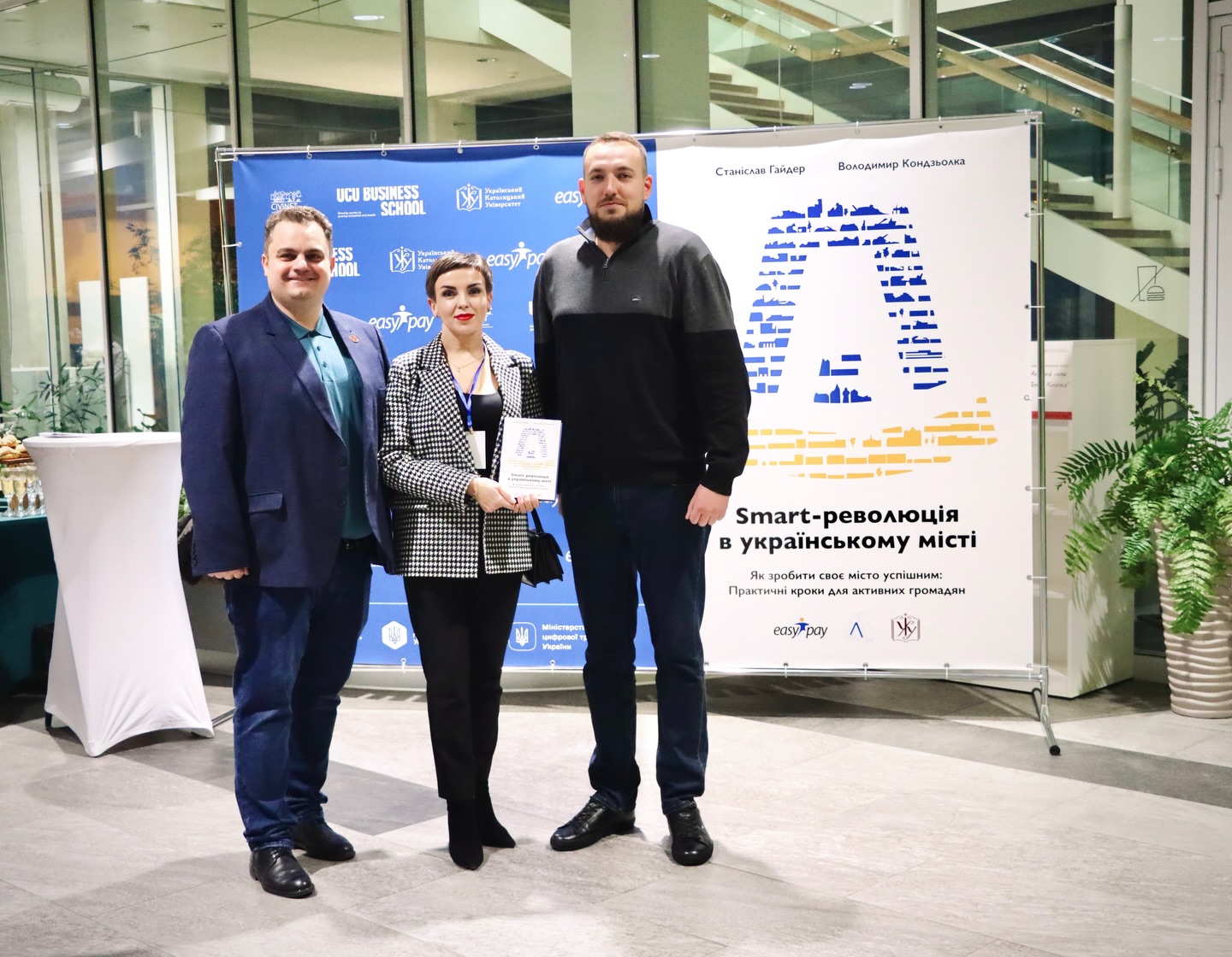 Два чоловіка та жінка стоять на фоні банера.