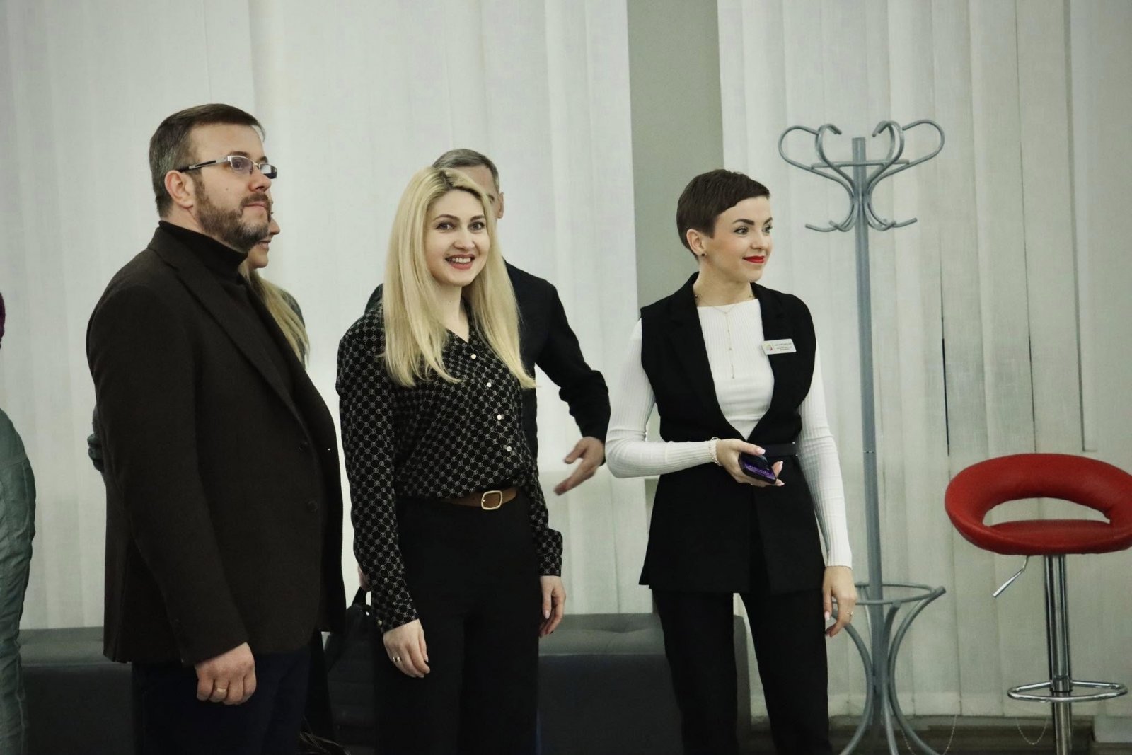 Кілька людей спілкуються у просторому приміщенні з білими шторами.
