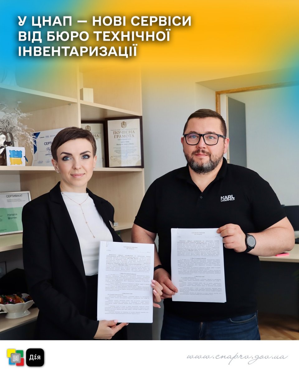 Чоловік і жінка стоять в офісі та тримають підписані документи, усміхаючись у камеру.