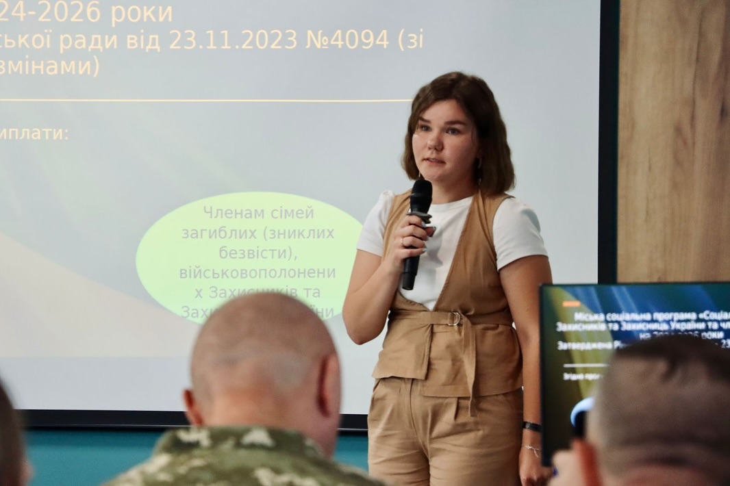 Жінка з темним волоссям говорить у мікрофон перед аудиторією.